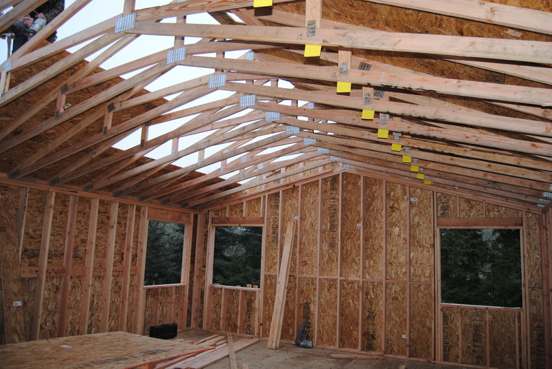 View up through the trusses at the worker as he adds plywood. View through the northeast corner of the room.