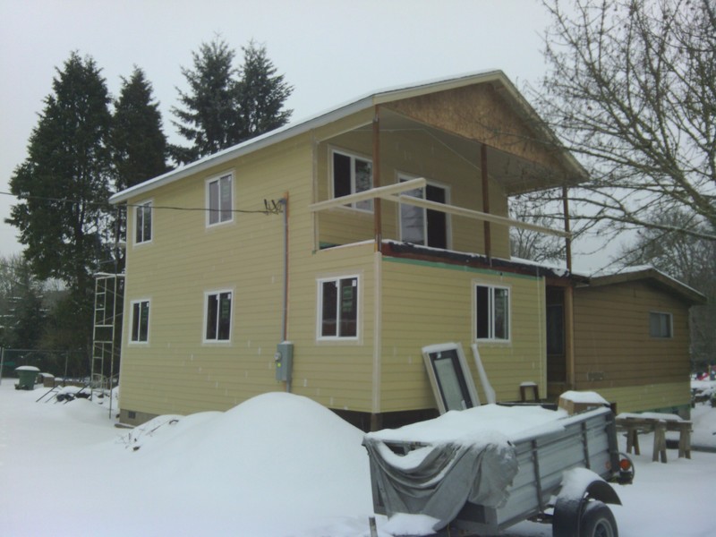 Snow surrounds the new addition. View of the northwest corner and balcony. New front door leans against the house.