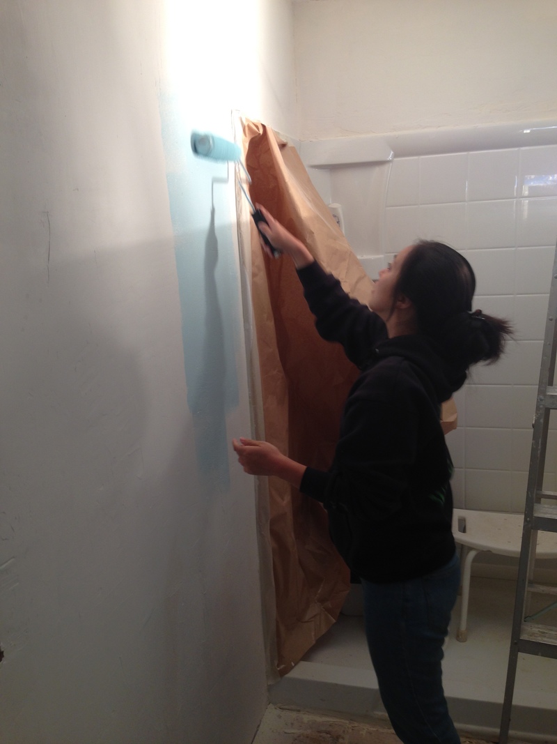 Akiko painting the bathroom wall with light blue paint.