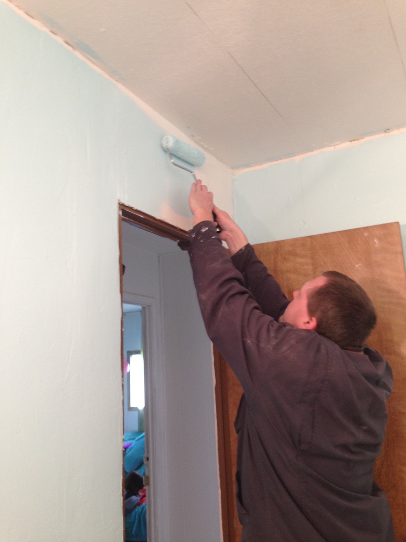 Joseph painting the bathroom wall with light blue paint.