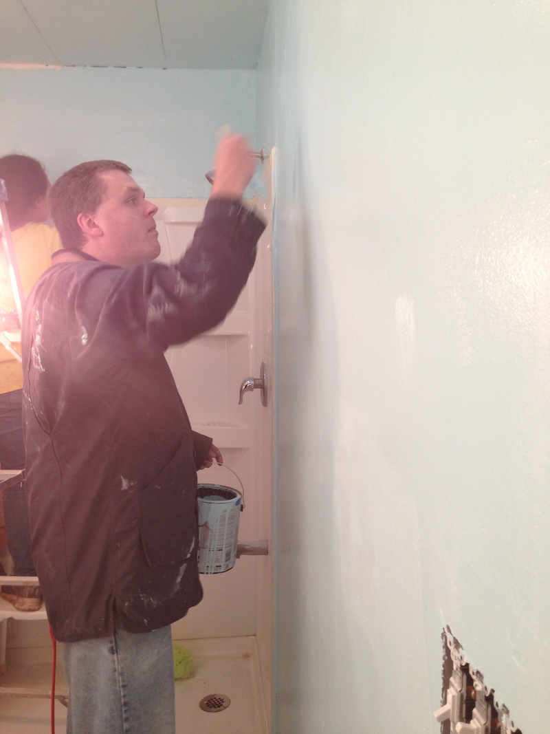 Joseph painting the bathroom wall with light blue paint.