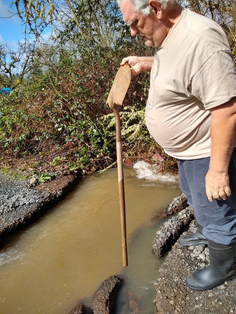 Tue 10:57 Culvert Gully. Don dips the shovel handle into the water to see how deep it runs.