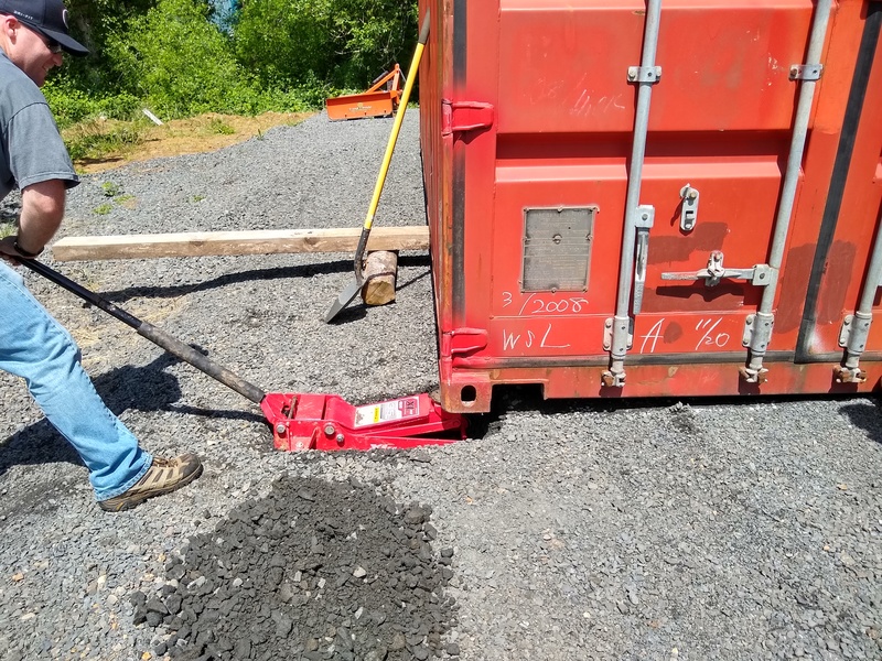 Mike Frankel mans a 3.5 ton hydraulic jack to raise the corner of the 2.4 ton A-Con container. He dug a hole in the gravel to get the jack under the corner.