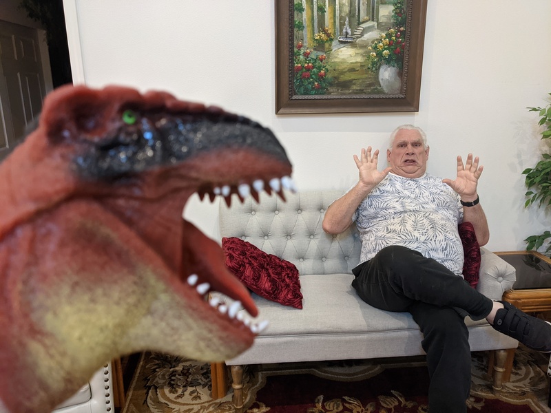 Lois is trying to scare Don with the dinosaur photo prop.
