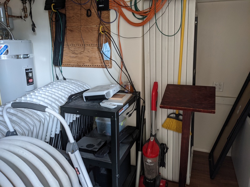 Here is a photo of the closet that is adjacent to the Great Room. You will notice eight banquet tables leaned up against a wall, and two rows of folding chairs. You can also see the projector, the lectern, and one of the water heaters. Just out of frame is the internet system.