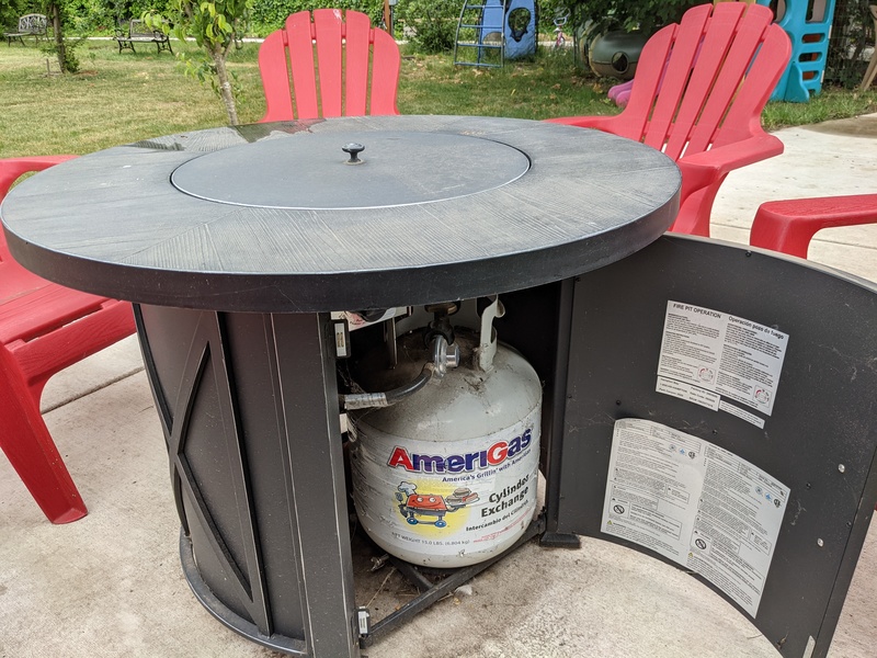 This is our gas-powered fire pit. It is in our Picnic Area. Here you can see it surrounded by red plastic adirondack chairs.