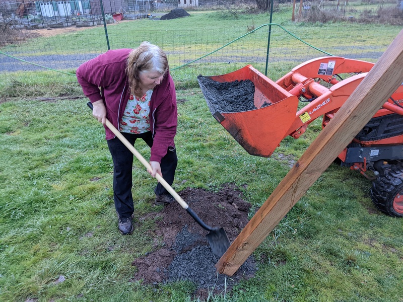 Lois is putting gravel into the holes for drainage to keep the post dry.