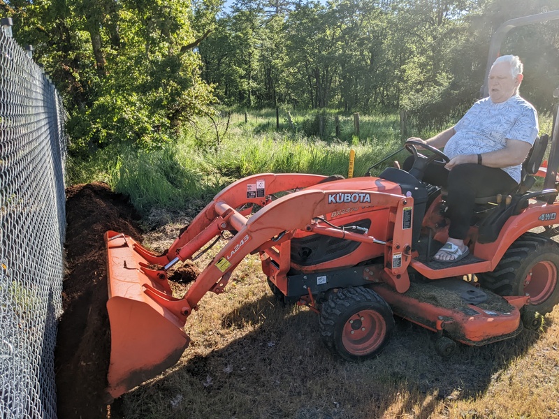 Don dumping bark along outside of East fence.