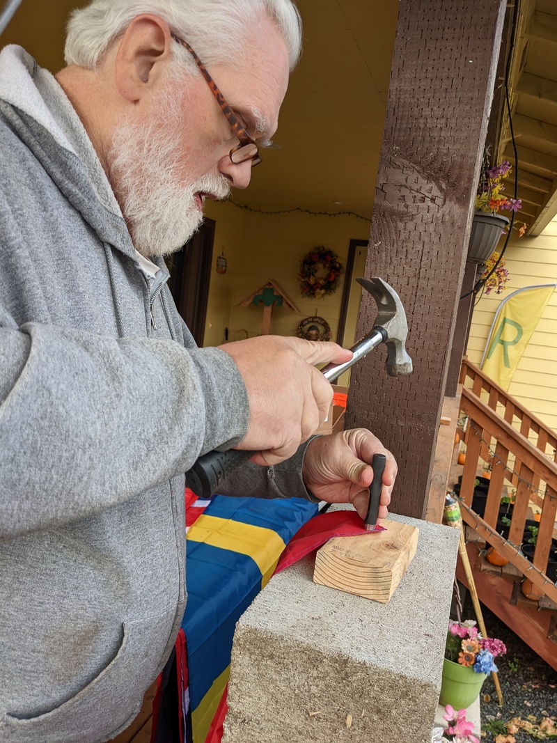 Don putting grommets in the 9 flags we got for The Firepit Village.